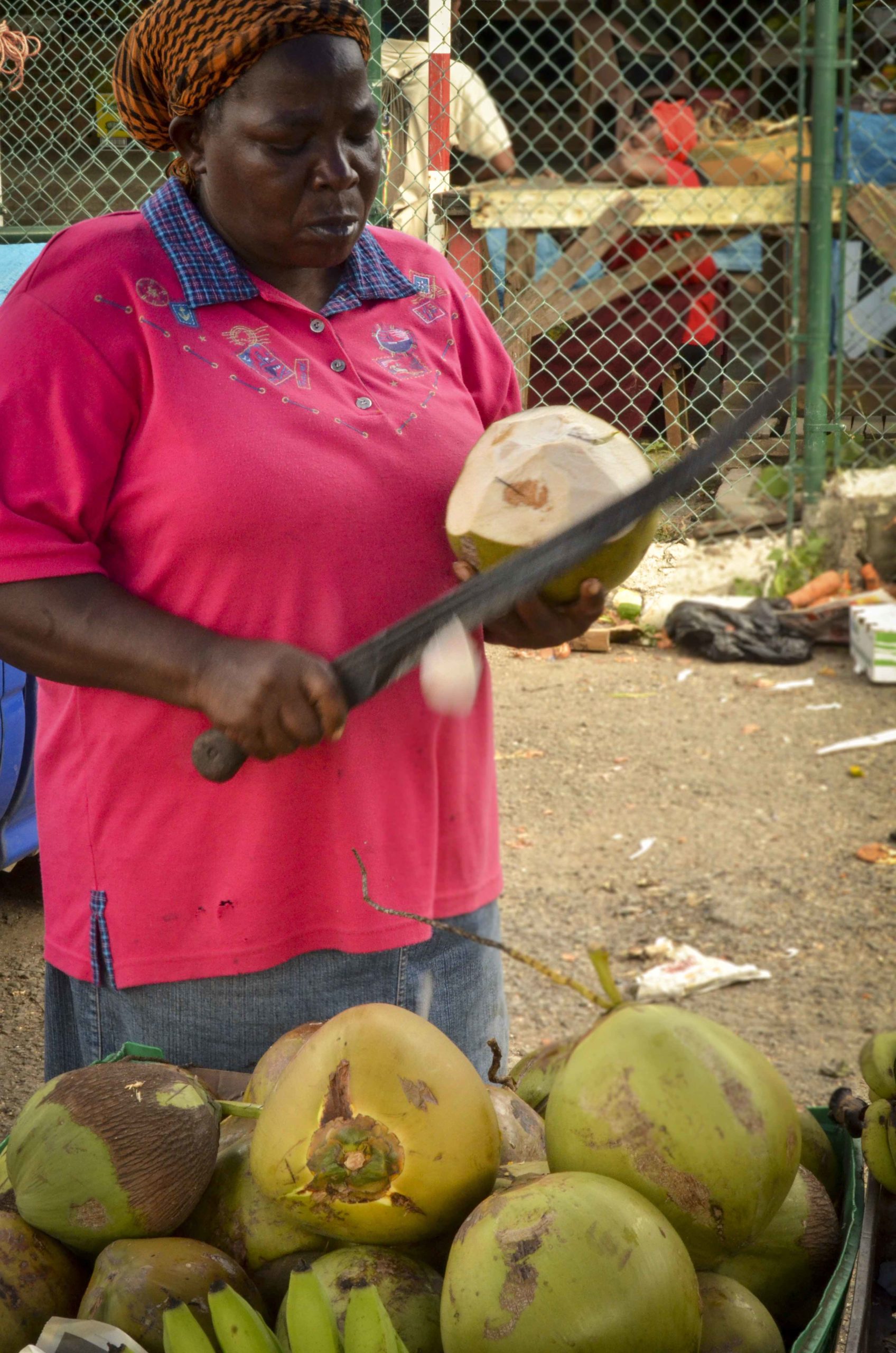 Femme utilisant une large lame pour trancher l'écorce verte du fruit.