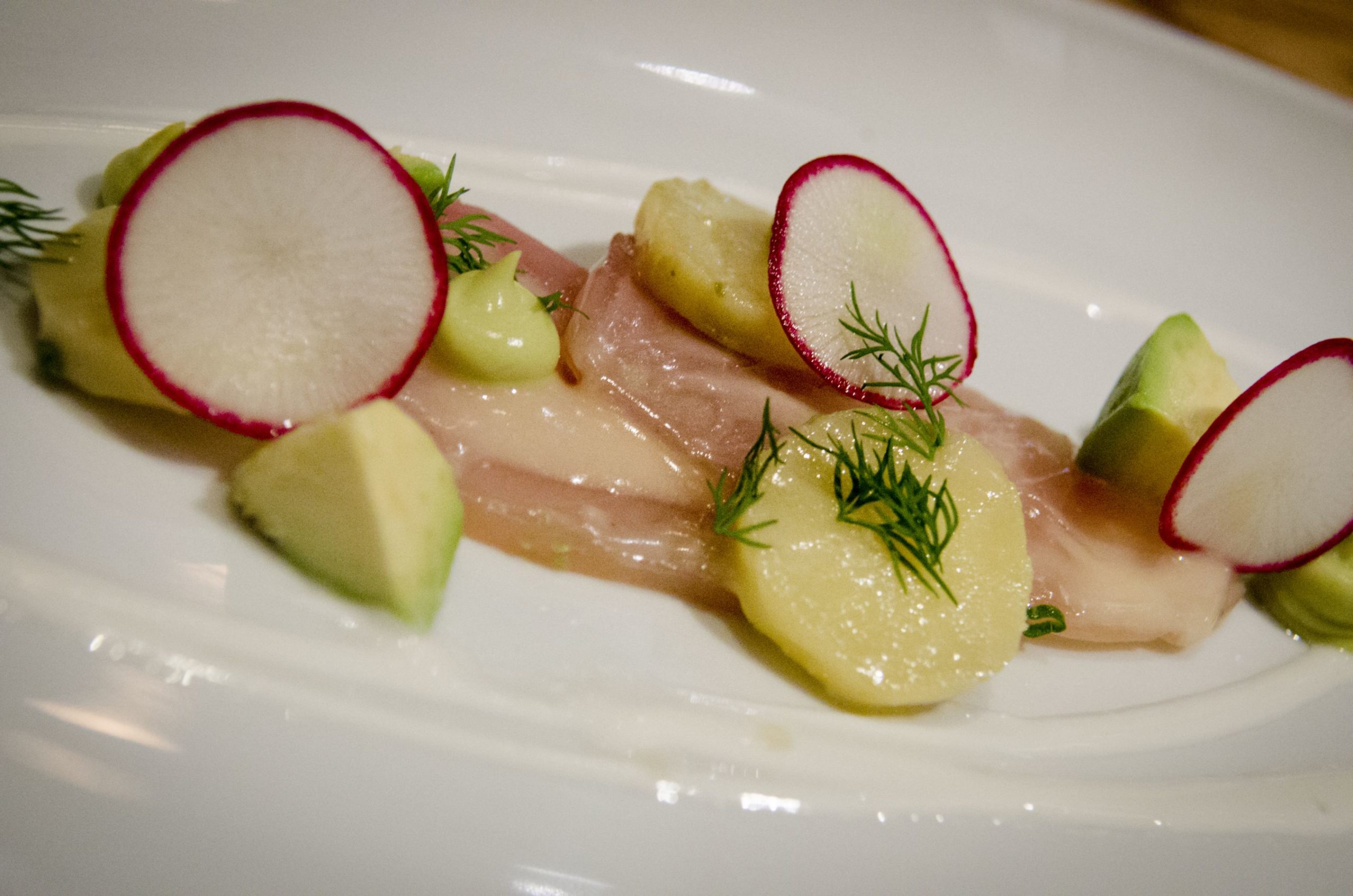 Morceaux de poisson partiellement saisis déposés sur une purée ou salade.